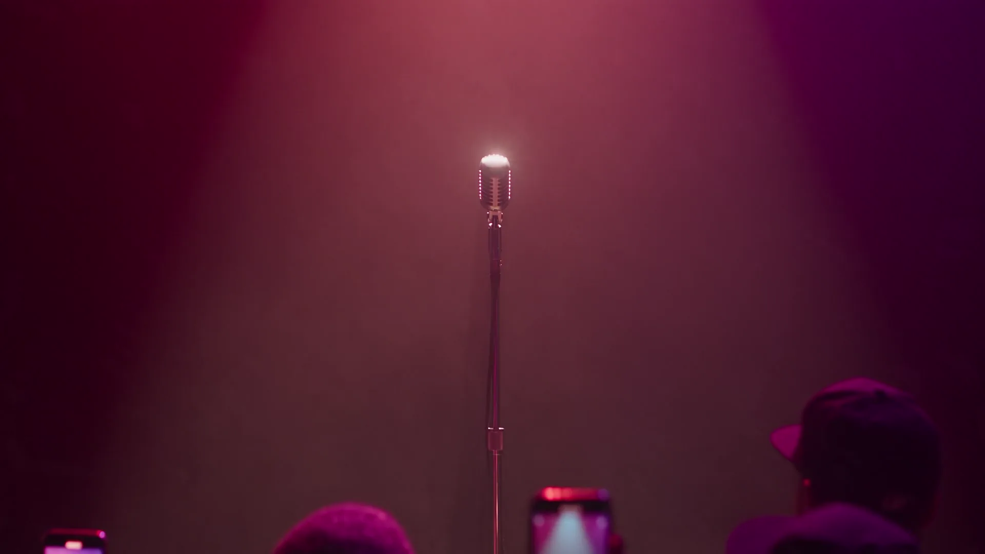 A chrome microphone alone on a stage under a red spotlight
